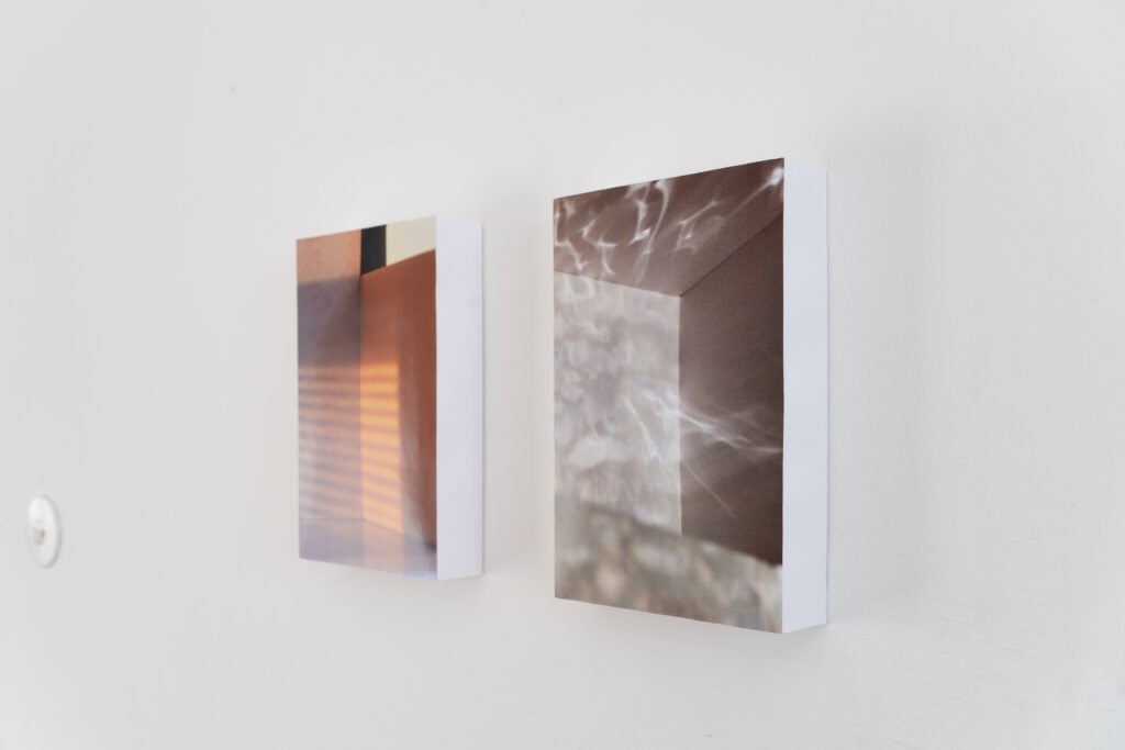 The two photographs from an angle. Here it becomes apparent the photographs are mounted on paper boxes, which gives them depth contrasting the flatness of the image plane.